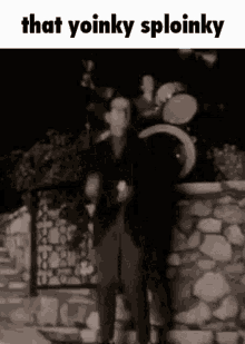 a man in a suit is standing in front of a stone wall with drums in the background .