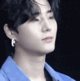 a young man wearing a blue shirt and earrings is looking at the camera .