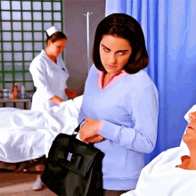 a woman in a blue sweater holds a black briefcase in front of a man in a hospital bed