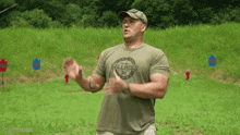 a man in a ballistics shirt is standing in a field with his hands outstretched .
