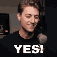 a man is smiling in front of a microphone and the word yes is on the screen