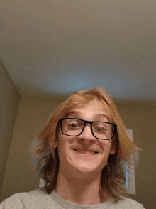 a young man wearing glasses and a grey shirt is smiling