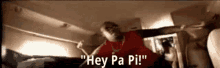 a man in a red shirt is standing in a room and saying hey pa pi !
