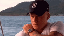 a man wearing a ny hat and a watch looks at the water