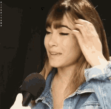 a woman in a denim jacket is holding a microphone in front of her