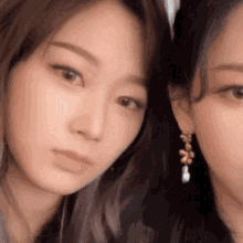 two women are standing next to each other and looking at the camera . one of the women is wearing earrings .