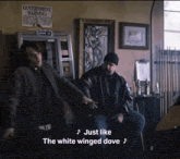 two men in a room with a government warning sign above them