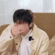 a man is sitting on a couch covering his mouth with his hand .