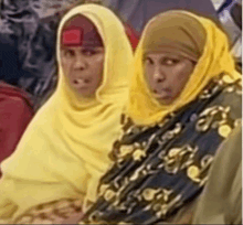 two women wearing yellow hijabs are sitting next to each other .