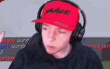 a young man wearing headphones and a red hat is sitting in front of a computer screen .