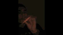 a man is smoking a cigarette in the dark with a red light behind him