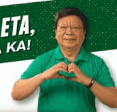 a man in a green shirt makes a heart shape with his hands