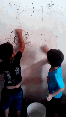 two boys are drawing on a white board and one of them is wearing a shirt that says ' designs ' on it