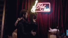 a man and a woman are hugging in front of a neon sign that says rock 'n ' roll