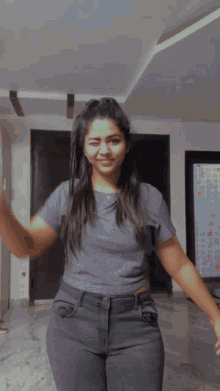 a woman in a grey shirt and black jeans is dancing in a room