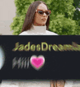 a woman wearing sunglasses and a white turtleneck is holding a sign that says jade dream .