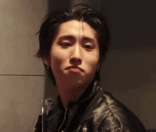 a young man wearing a black leather jacket is making a face .