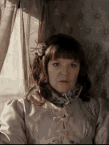 a woman with a flower in her hair is sitting in front of a window with the words made with reface app on the bottom