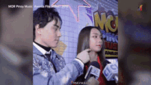 a man is touching a woman 's face in front of a sign that says ' mor pinoy music awards '