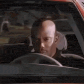 a bald man is sitting in the driver 's seat of a car looking at the camera