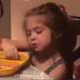 a little girl is sitting at a table with a yellow plate and a toy .