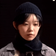 a close up of a woman wearing a beanie and scarf making a funny face .