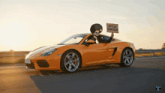 a man in an orange sports car holds up a sign that says official ambassador