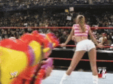 a woman in a pink top and white shorts is dancing in a wrestling ring with a wwe logo in the background