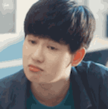 a young man wearing a blue jacket and a green shirt is looking at the camera .