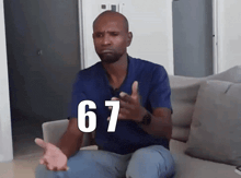 a man in a blue shirt is sitting on a couch with the number 67 on his shirt