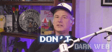 a man wearing a purple hat stands in front of a microphone with the words " do n't dark web " on the screen