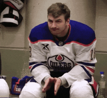 a man wearing a blue white and red oilers jersey sits on a bench