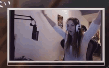 a woman wearing headphones is sitting in front of a microphone with her arms outstretched .