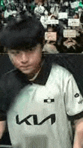 a young boy wearing a white ktm jersey is standing in front of a crowd .