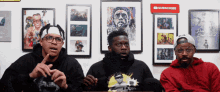 three men are sitting in front of a wall with pictures on it and a sign that says subscribe