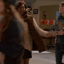 a woman wearing a sweater and a leopard print vest stands in a room with other people