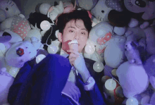 a man in a suit is laying in a pile of stuffed animals and eating ice cream