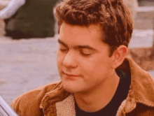 a young man wearing a brown jacket is looking down at something .