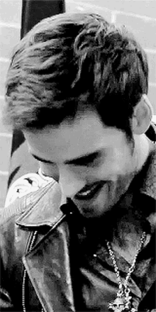 a close up of a man wearing a leather jacket and a necklace .