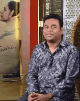 a man in a floral shirt is sitting in front of a sign that says ' yidai ' on it