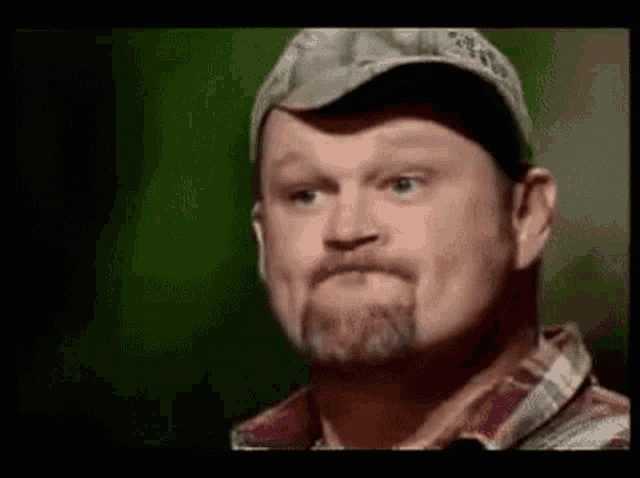 a man with a beard wearing a hat and a plaid shirt is making a funny face .